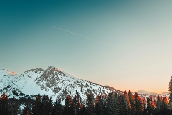 Landskapsbilde av et fjell med blå himmel i bakgrunn og skog nederst på bilde.